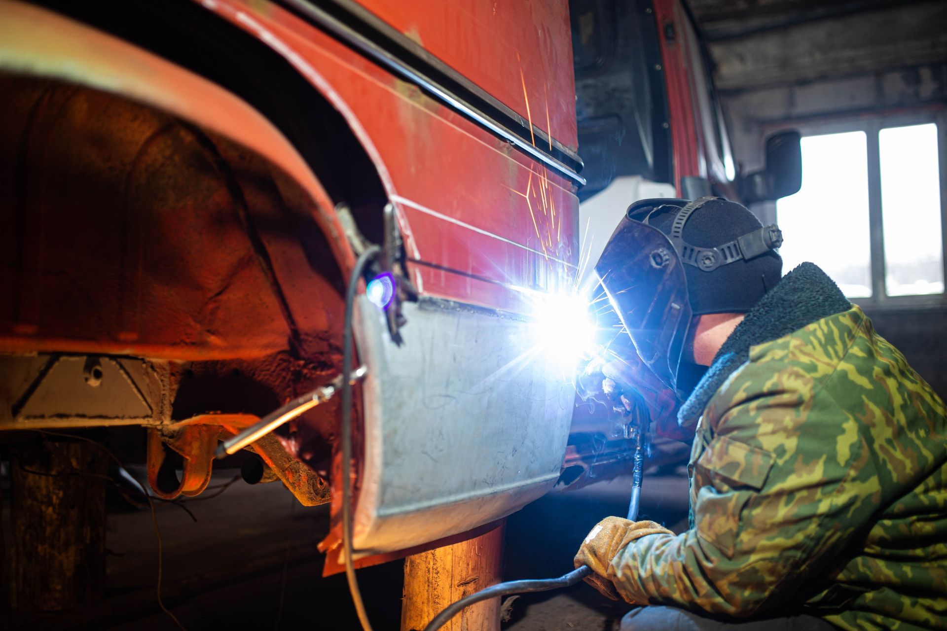 Person welding on a red vehicle in a garage, sparks flying.