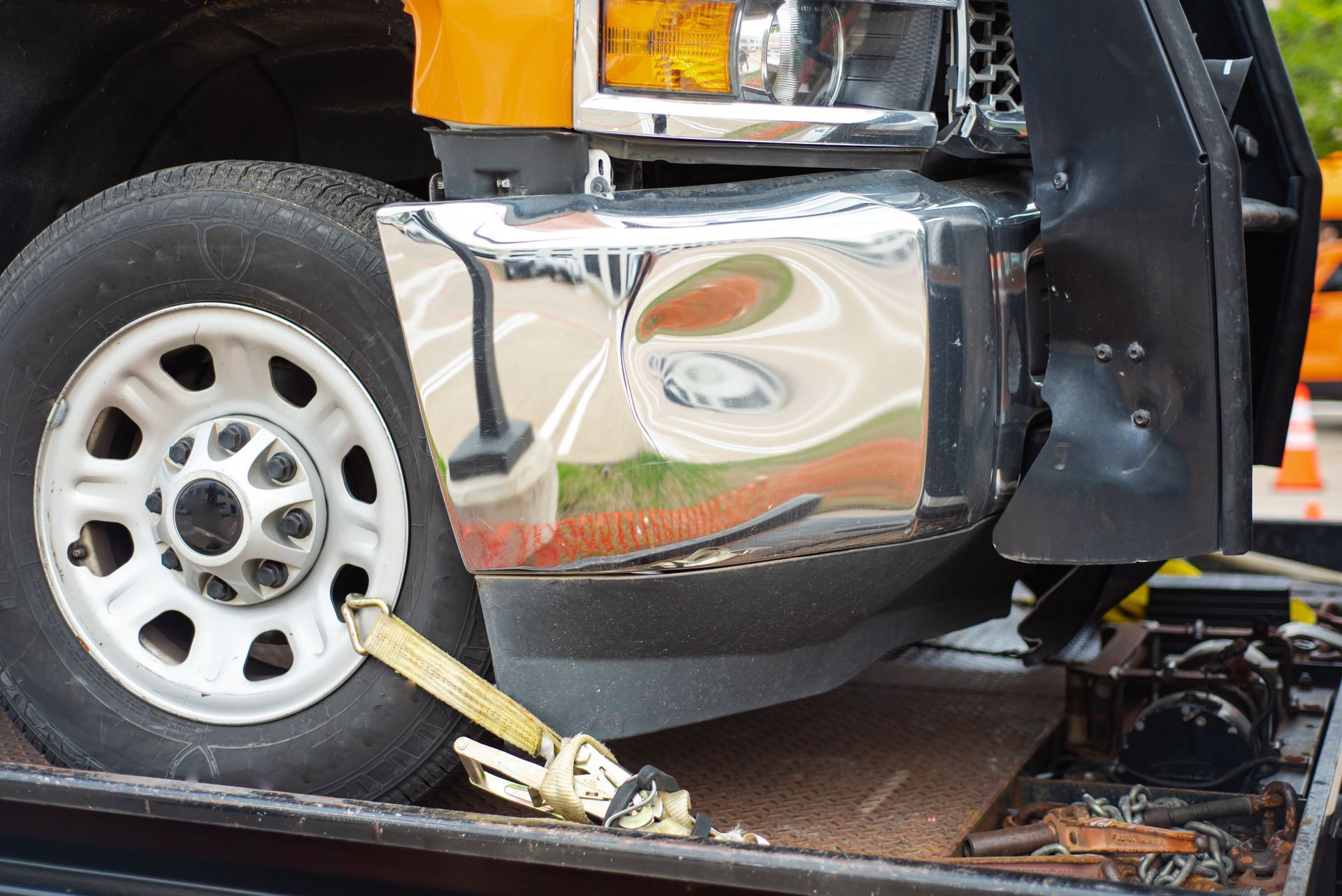 Damaged truck bumper with reflection, tire, and tow strap on a flatbed.
