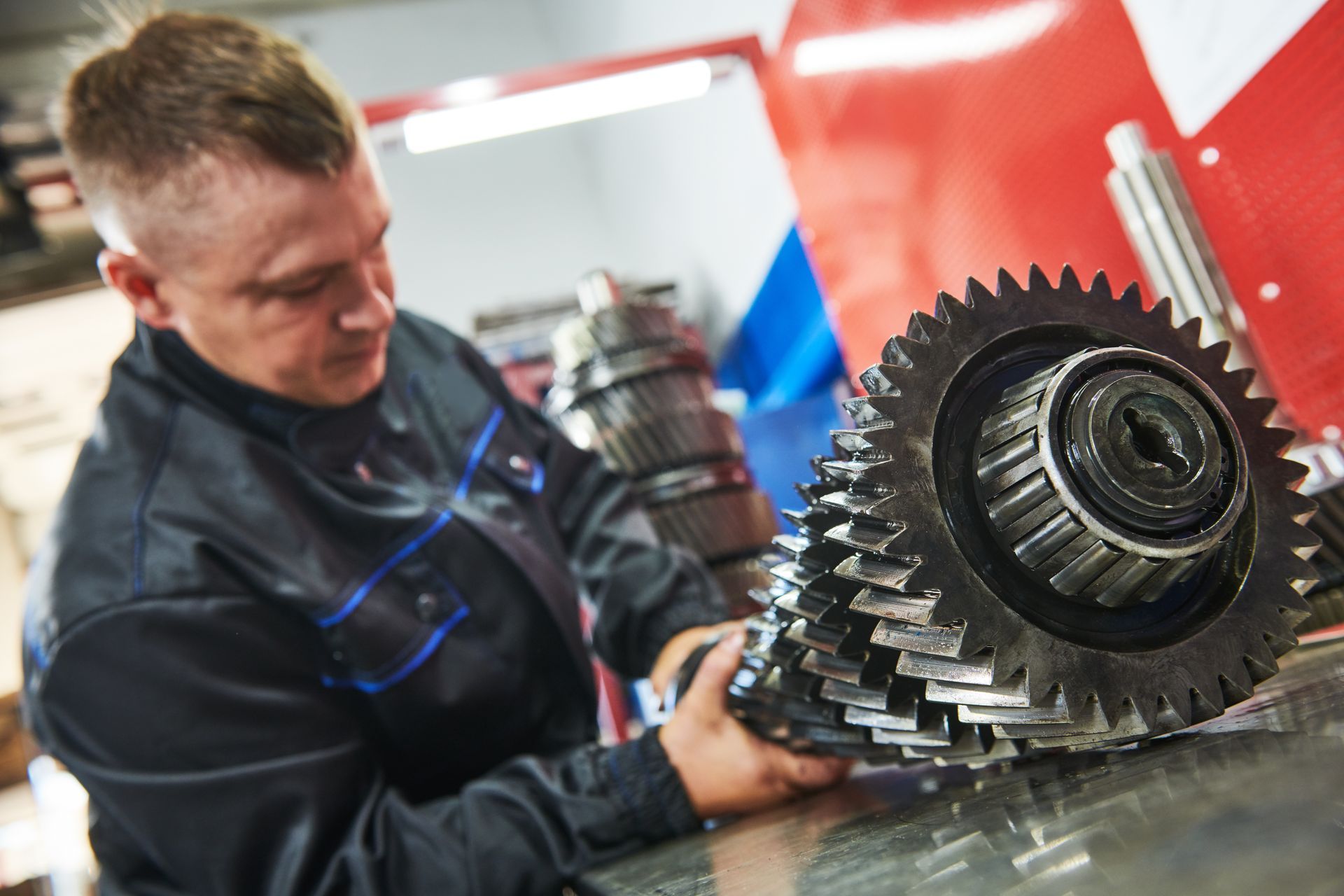 Mechanic holding gears, examining them on a workbench in a repair shop.