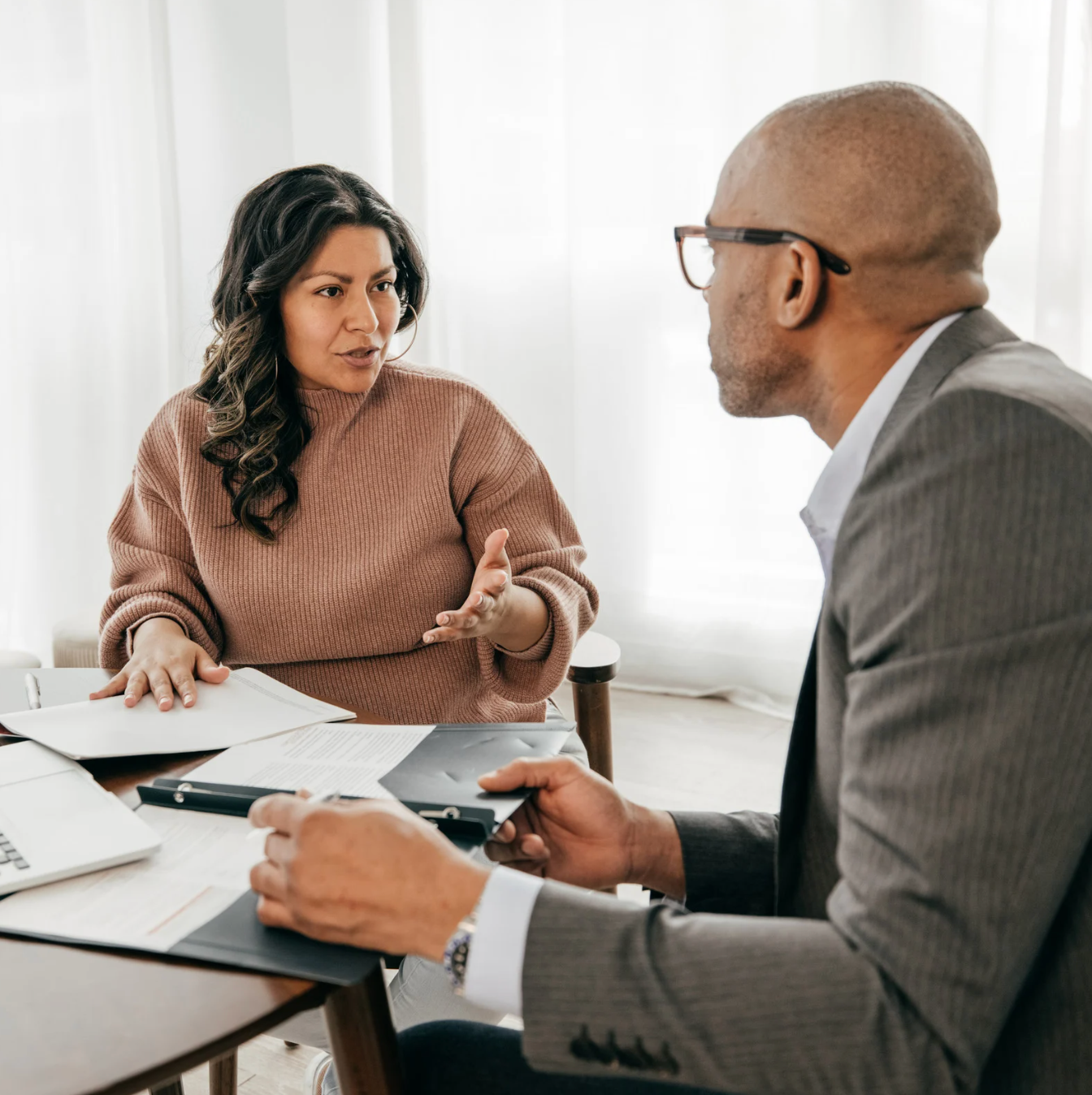 A woman is holding a red folder in front of a man holding papers A man and a woman are sitting at a table having a conversation.