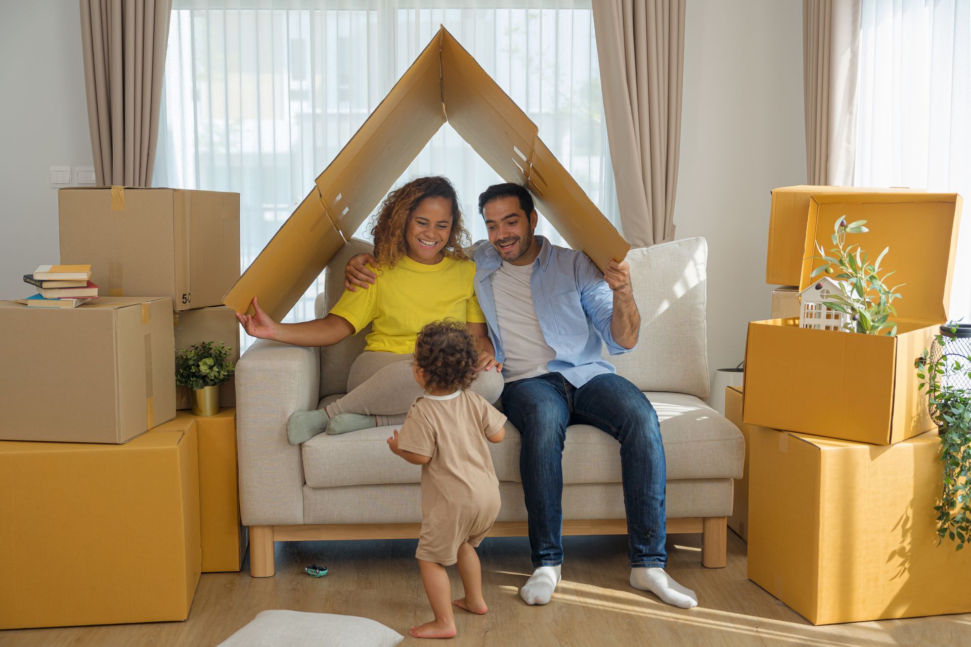 A family is sitting on a couch in a living room surrounded by cardboard boxes.