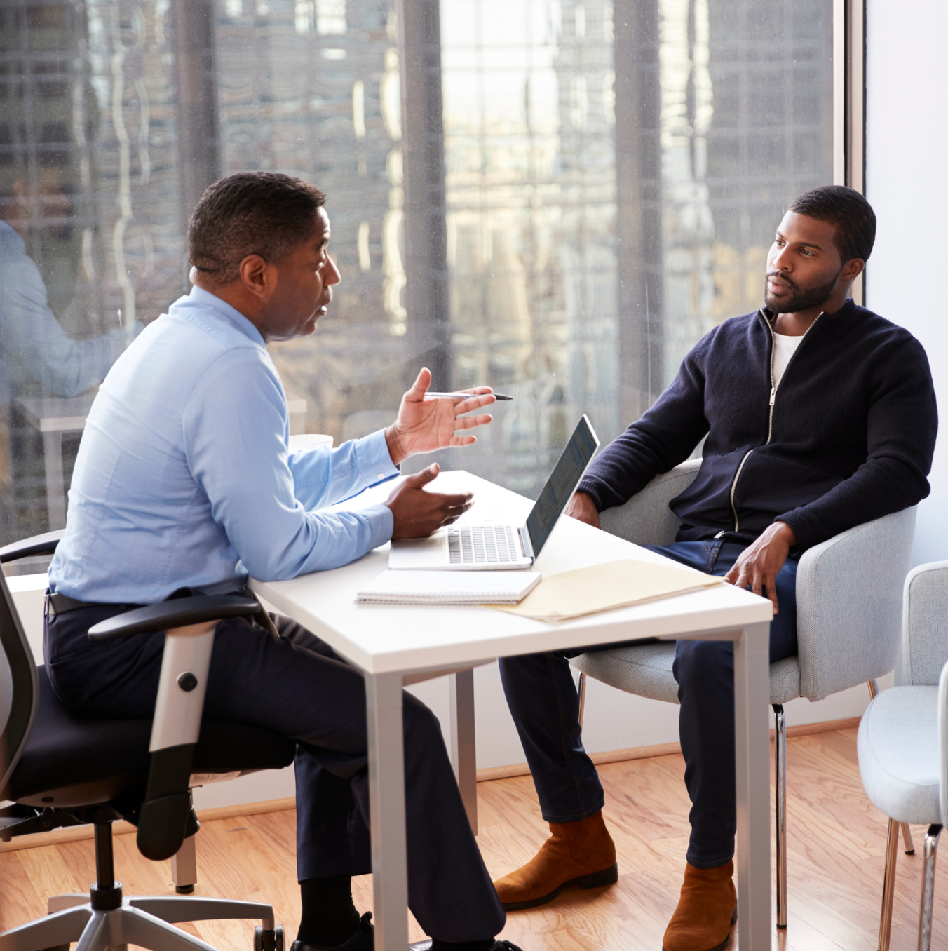 A woman wearing a colorful shirt and earrings smiles for the camera Two men are sitting at a table with a laptop and talking to each other