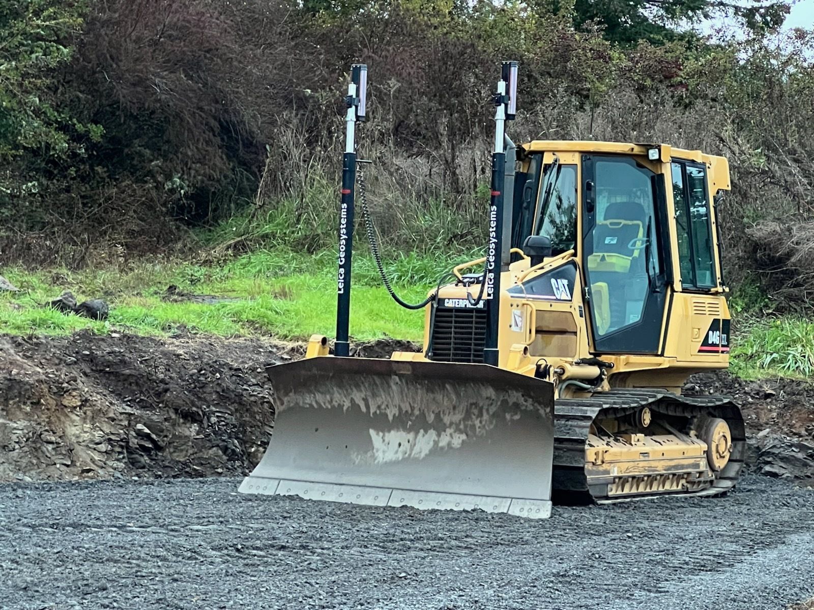 A yellow Caterpillar bulldozer with grade-control masts sits on a gravel construction site.