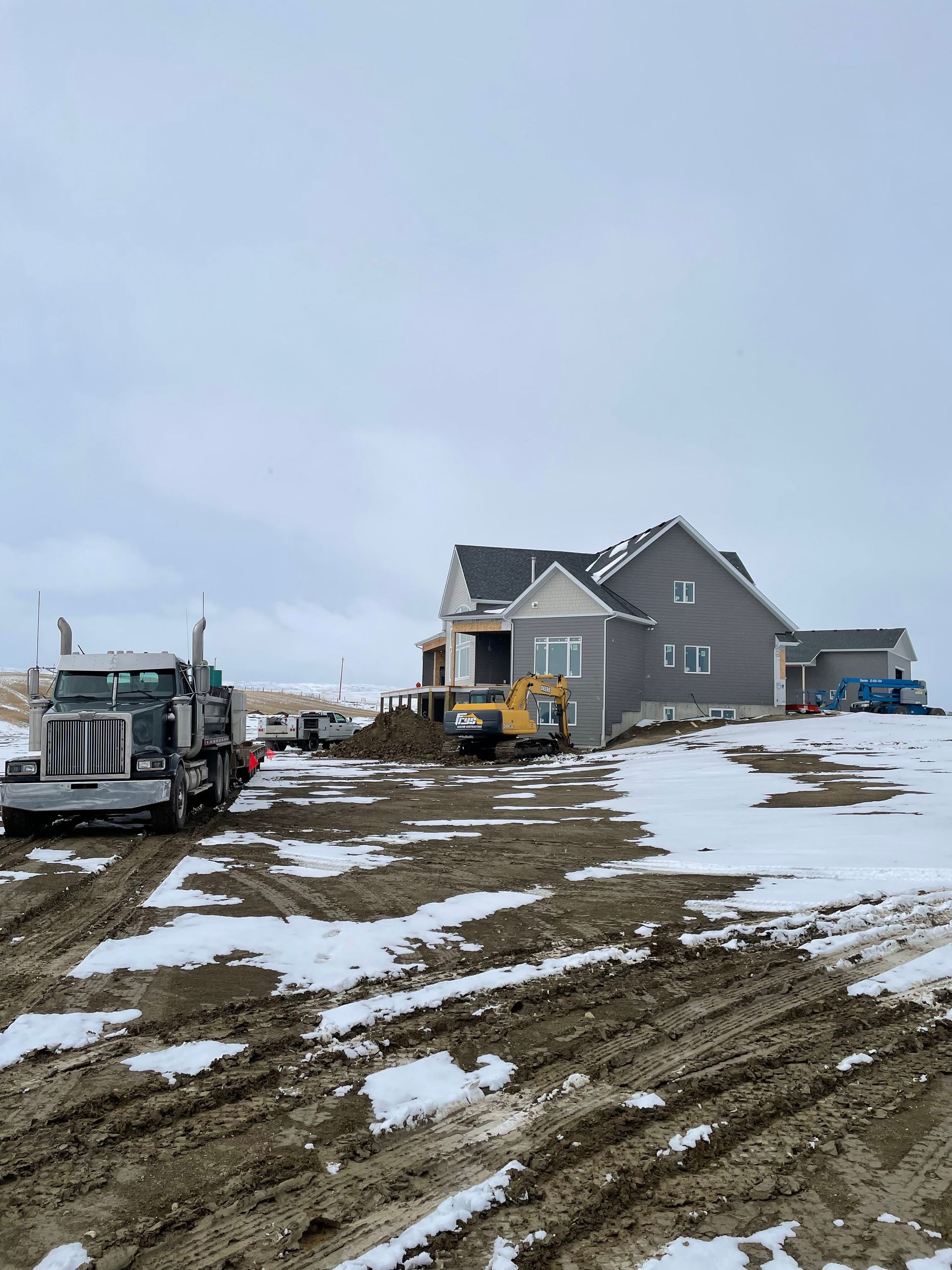 A truck is driving down a dirt road in front of a house.