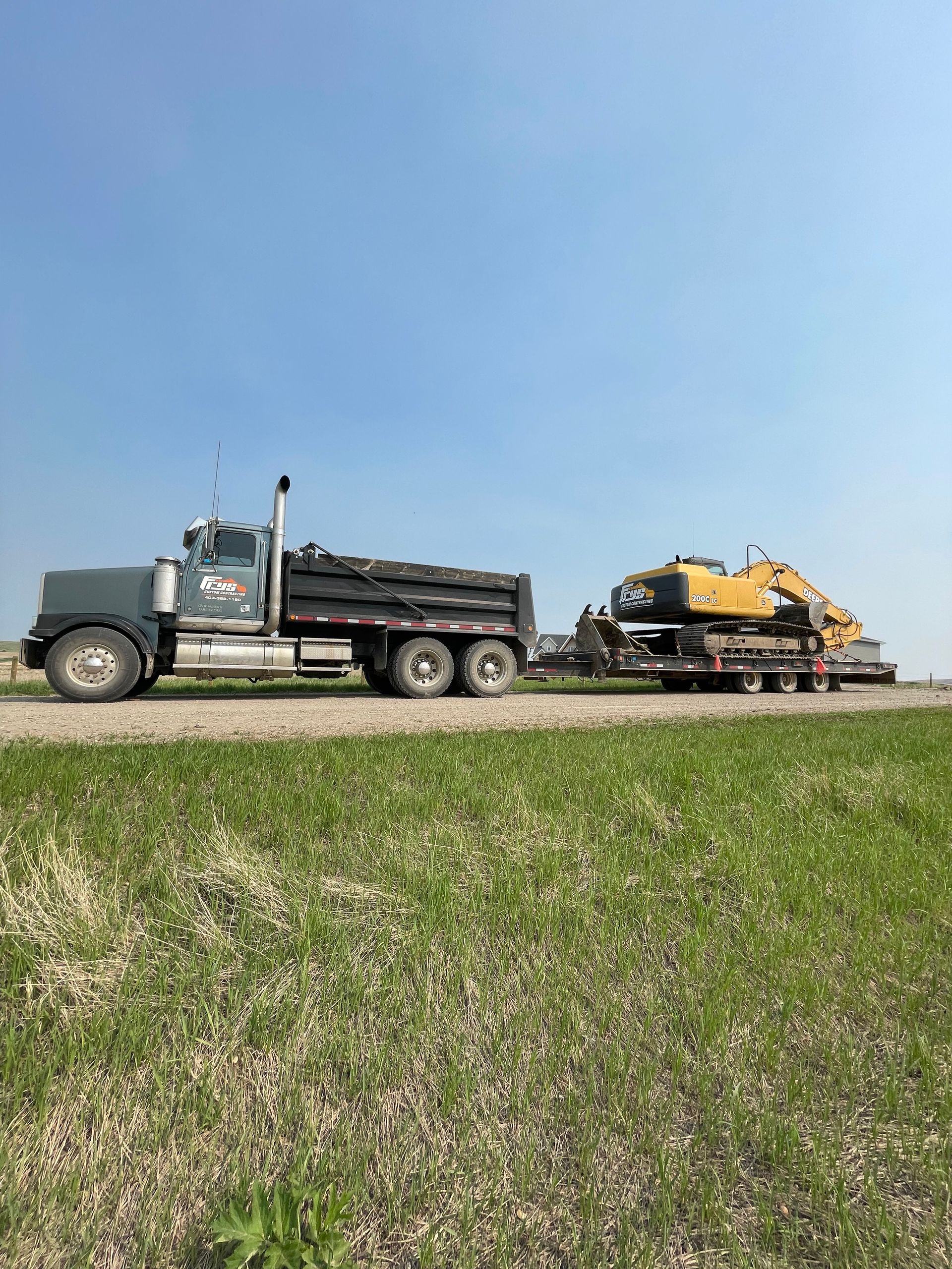 A dump truck is carrying a yellow excavator on a trailer.