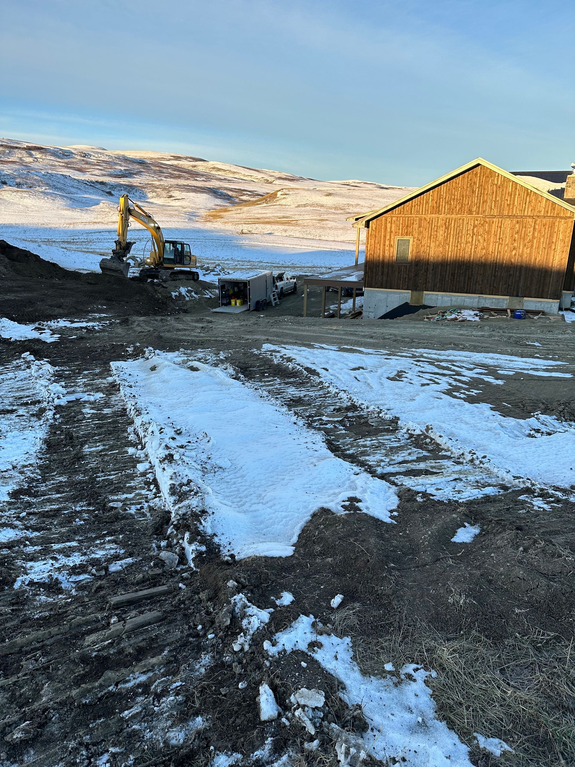 A construction site with a house in the background and snow on the ground.