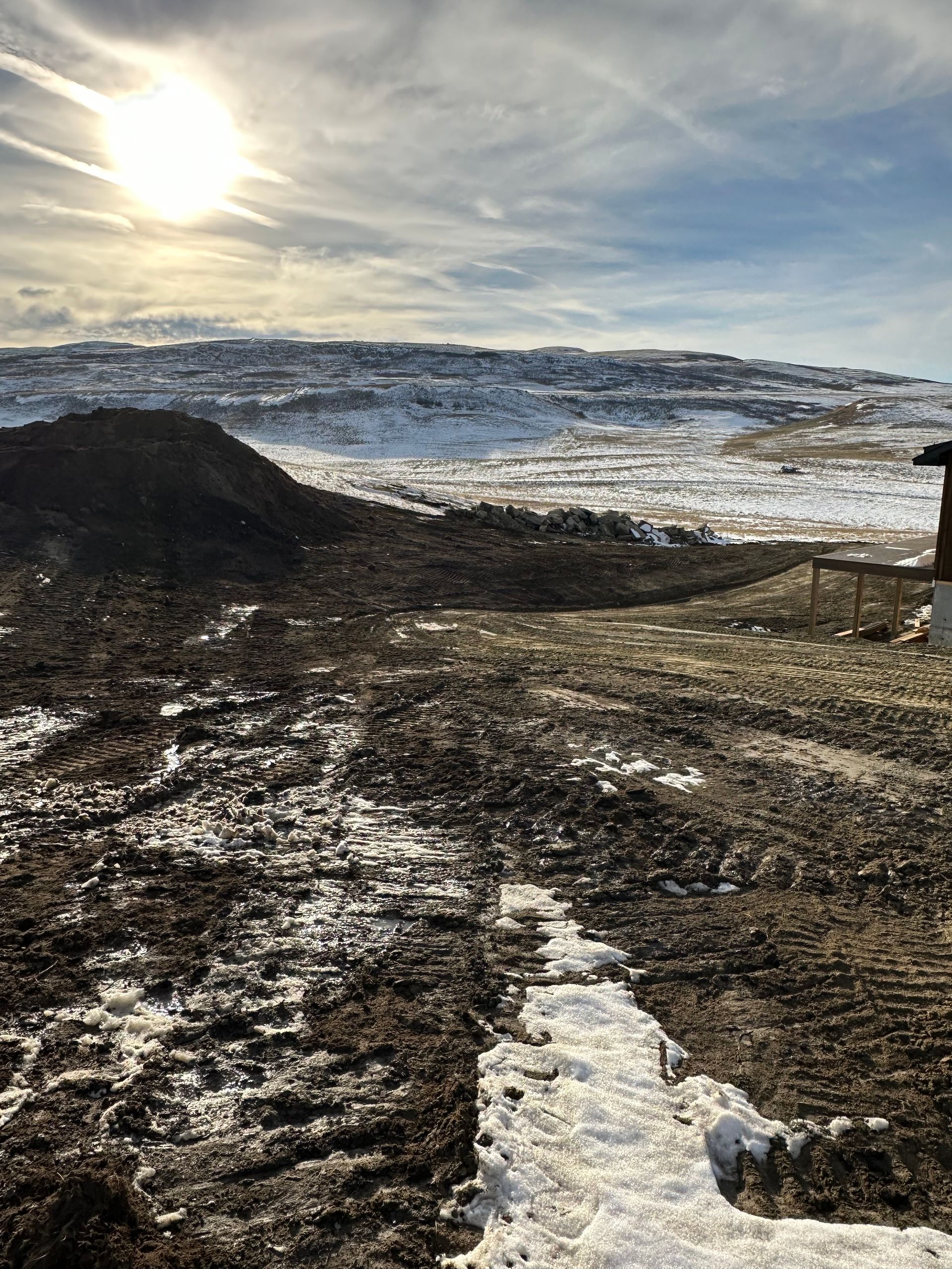 A muddy field with snow on the ground and a mountain in the background.