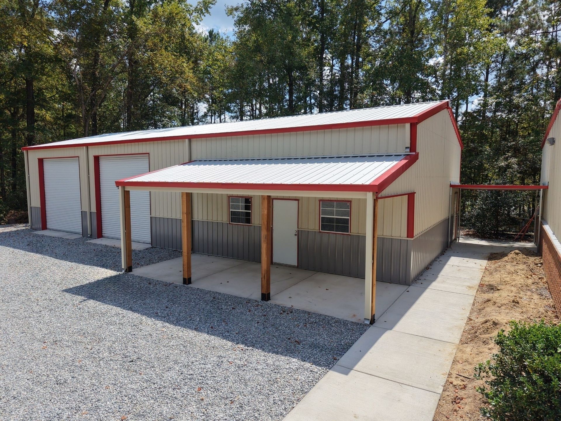 Metal building with a white and red roof, two garage doors, and a small porch.