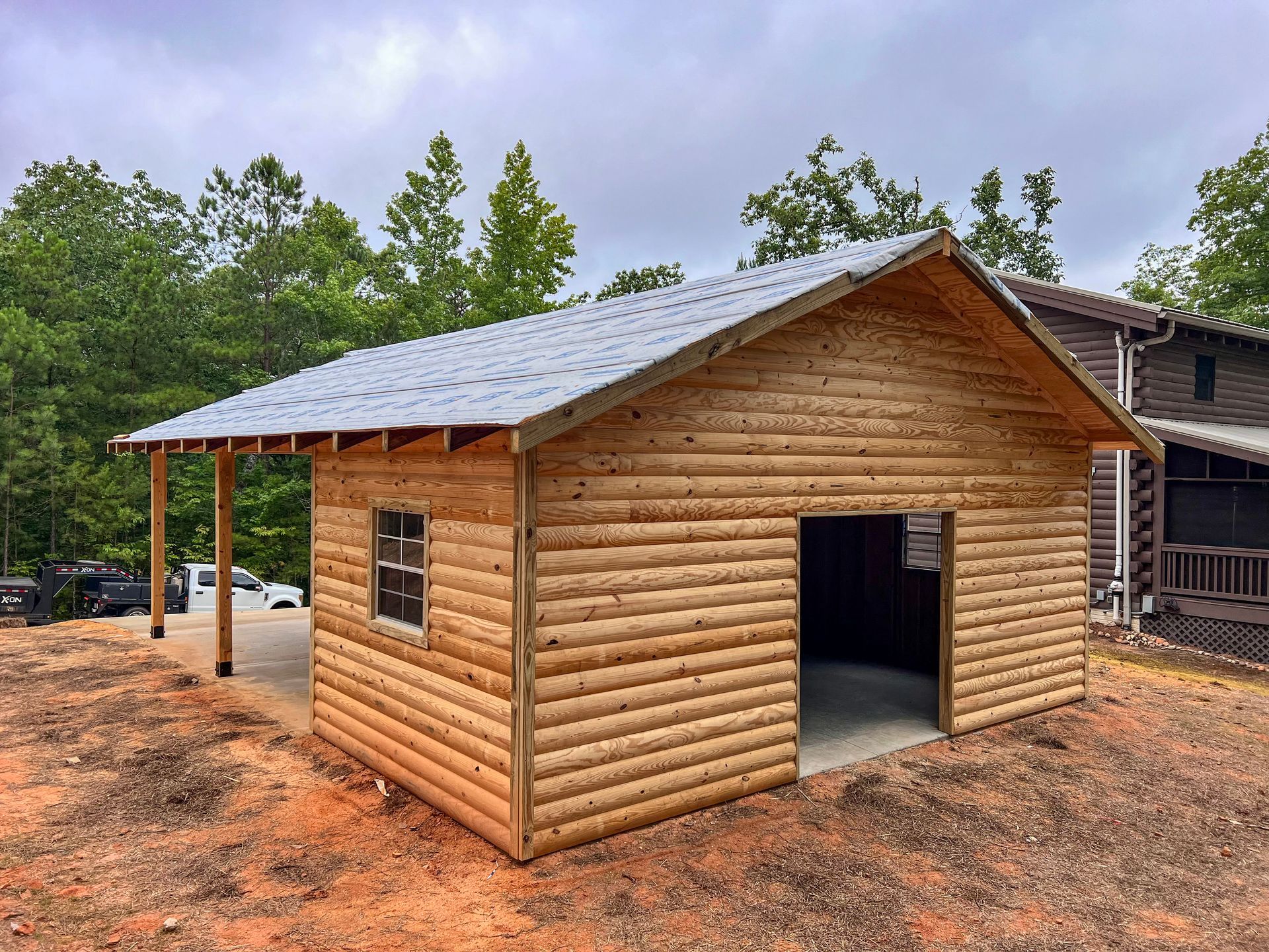 A log cabin with a metal roof is sitting in the middle of a dirt field.