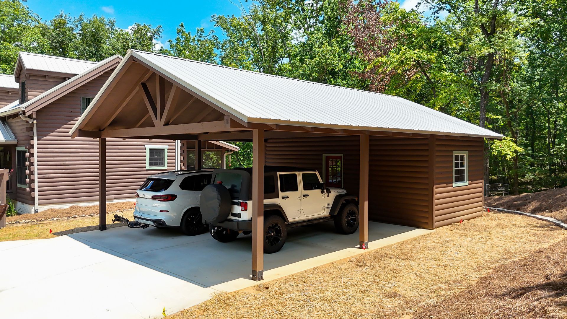 Two cars are parked under a carport in front of a house.