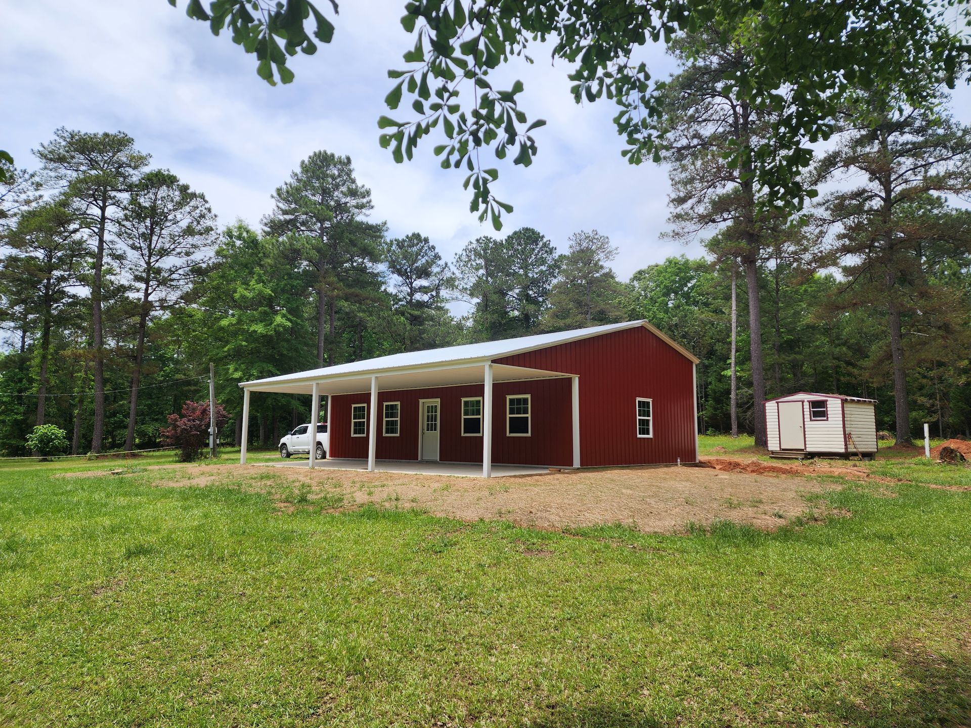 A red barn with a white porch is sitting in the middle of a grassy field.