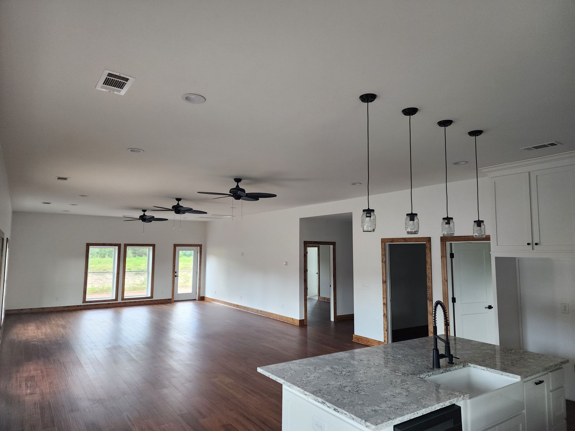 A large empty room with a kitchen and a ceiling fan.