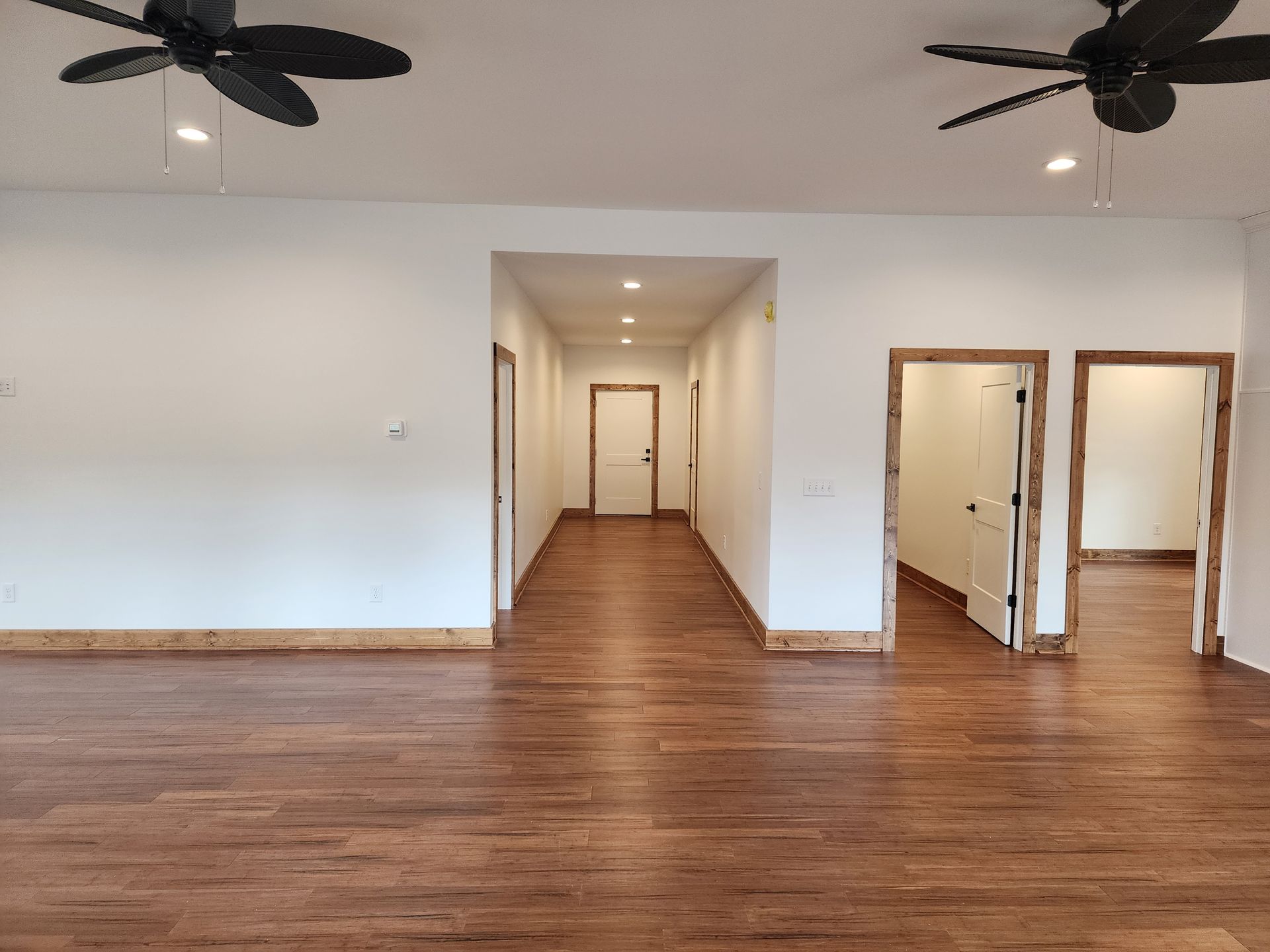 Empty room with hardwood floors, white walls, and a hallway with several doorways.