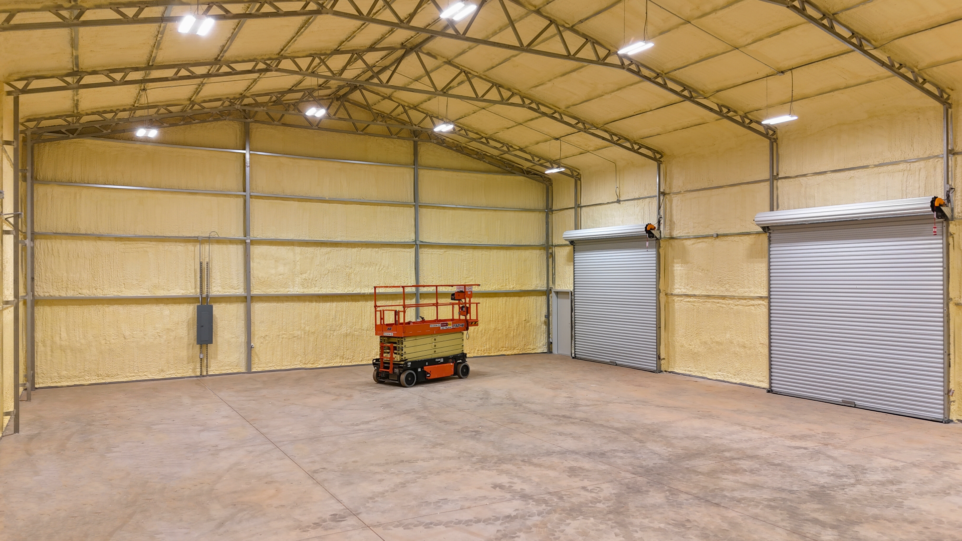 Inside view of a large warehouse with concrete floor, tan insulation, metal frame, and two closed roll-up doors.