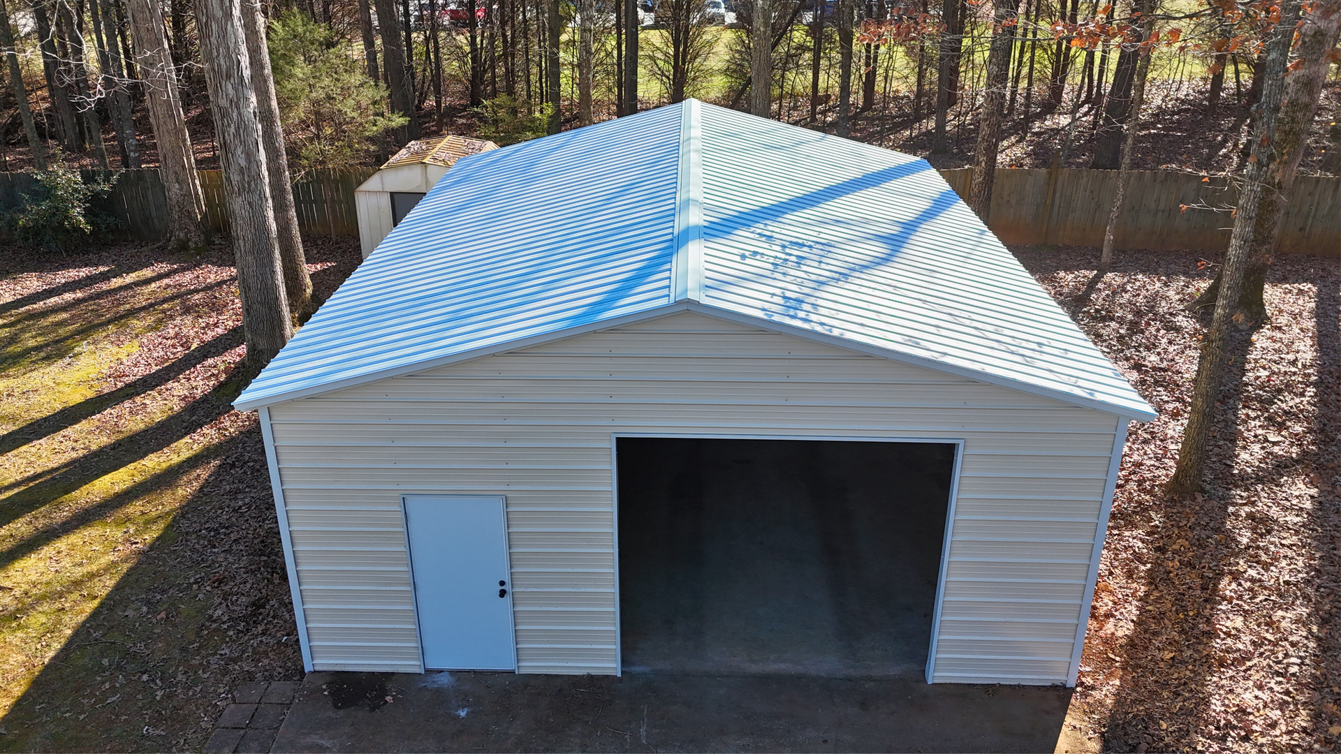 Metal garage with light blue door and corrugated roof, set in a wooded area.