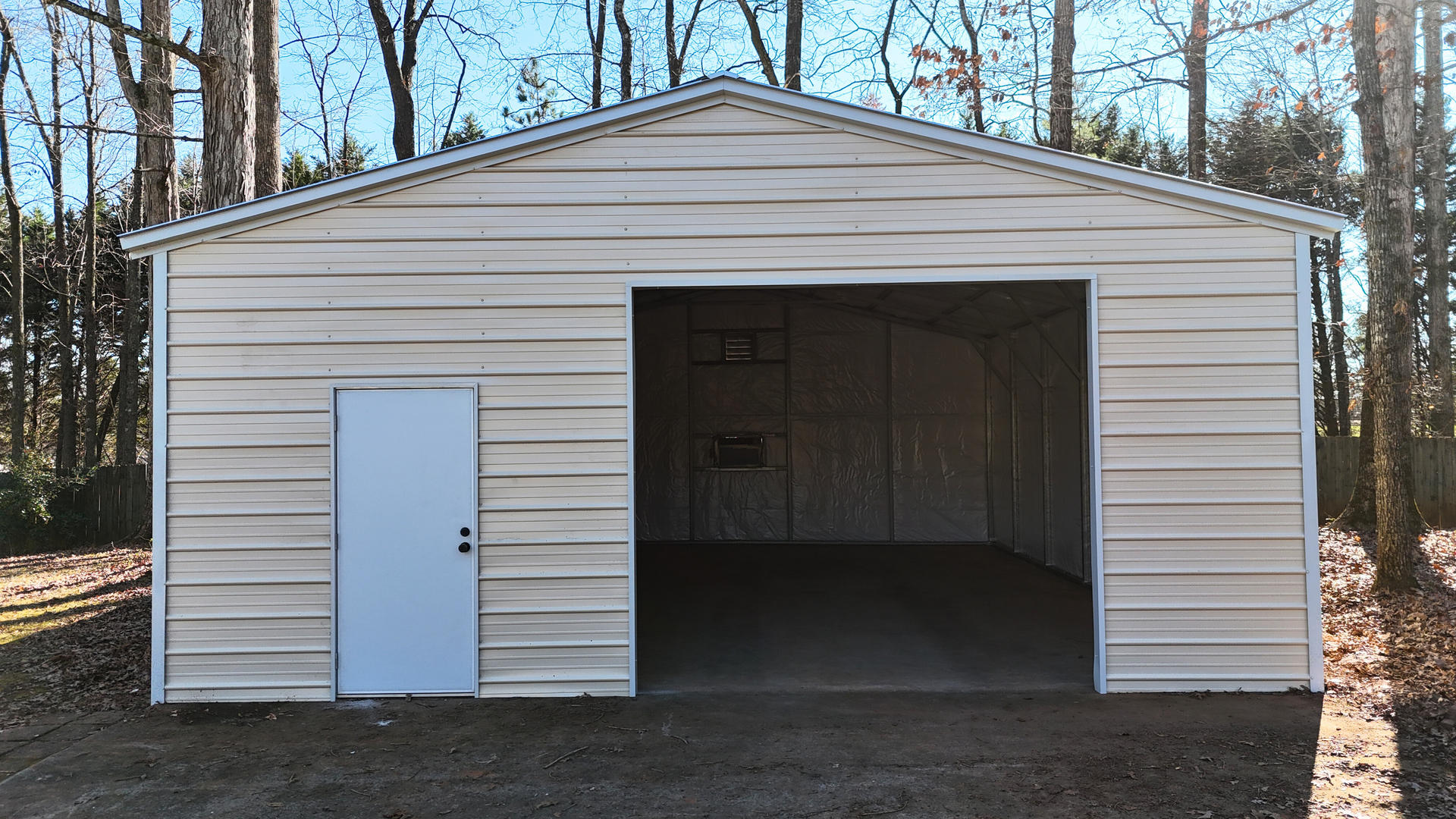 Beige metal garage with a large open entrance and a white side door, set among trees.