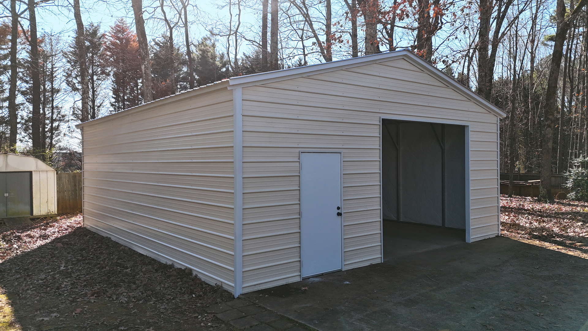 Beige metal building with open garage door, white door, gravel driveway.