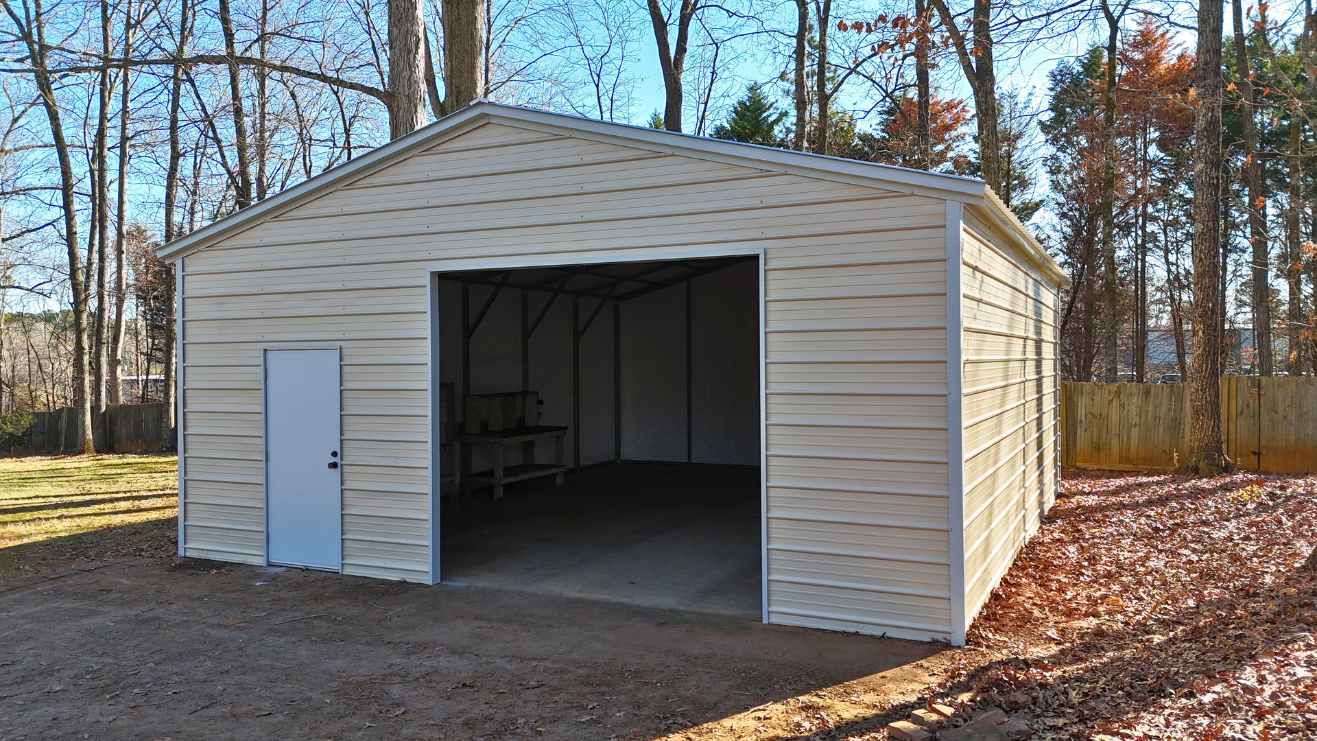 Tan metal garage with a large open entrance and a side door, set in a yard with trees.