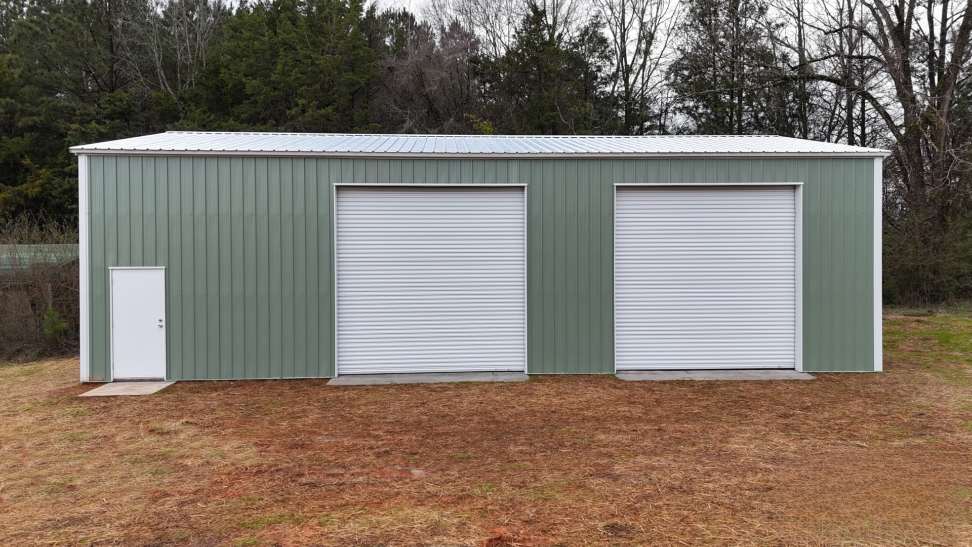 Green metal building with two garage doors and a small white door.