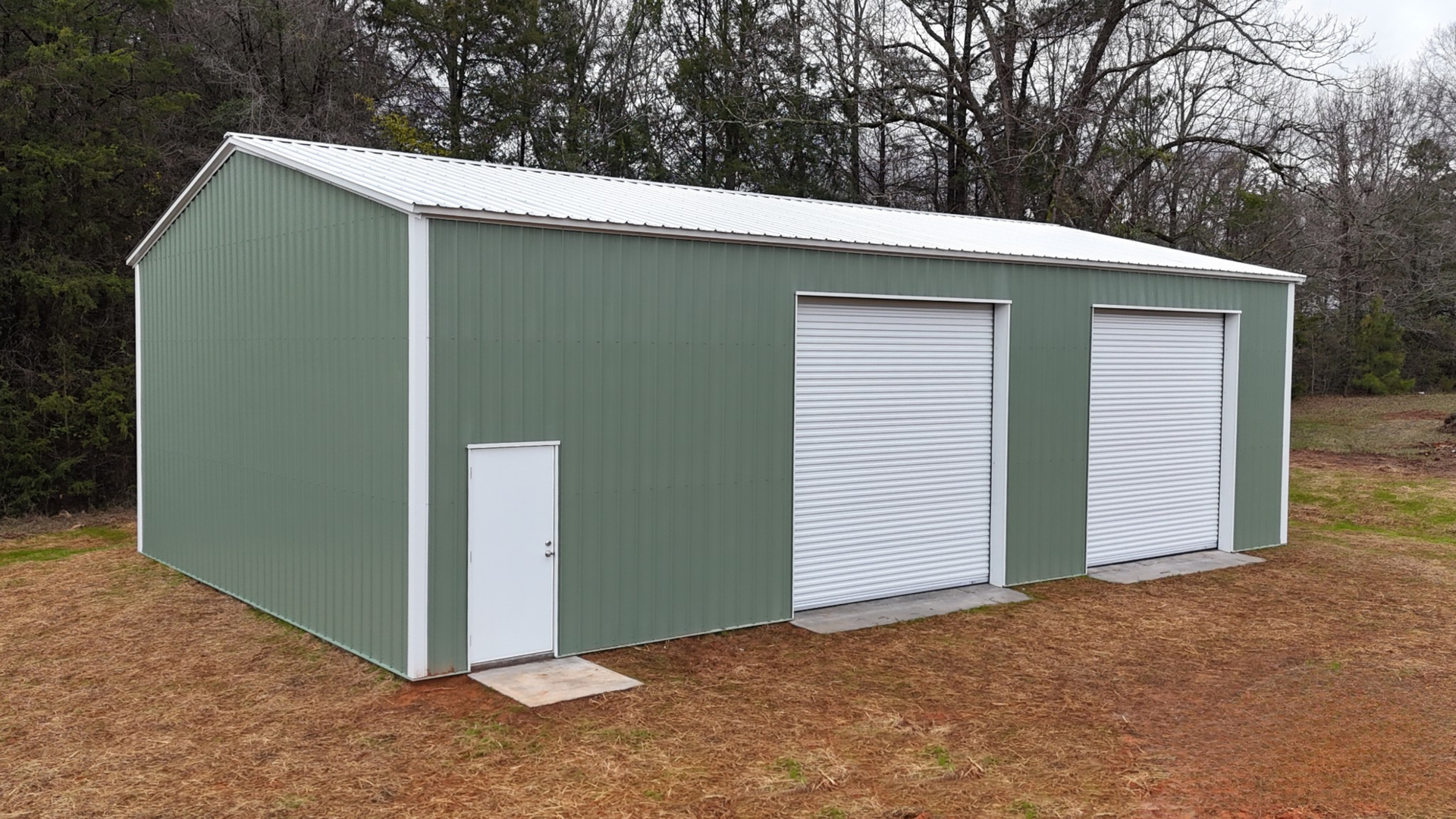 Green metal building with white doors and two garage doors.