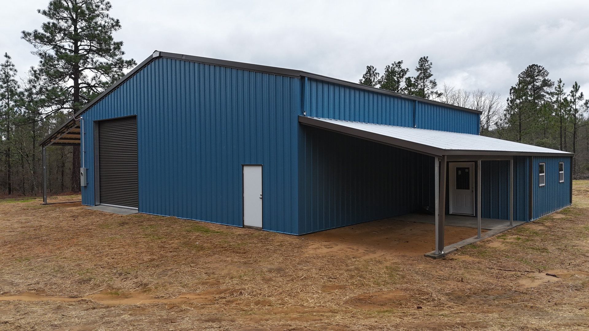 Blue metal building with a lean-to roof extension, a garage door, and a white door.