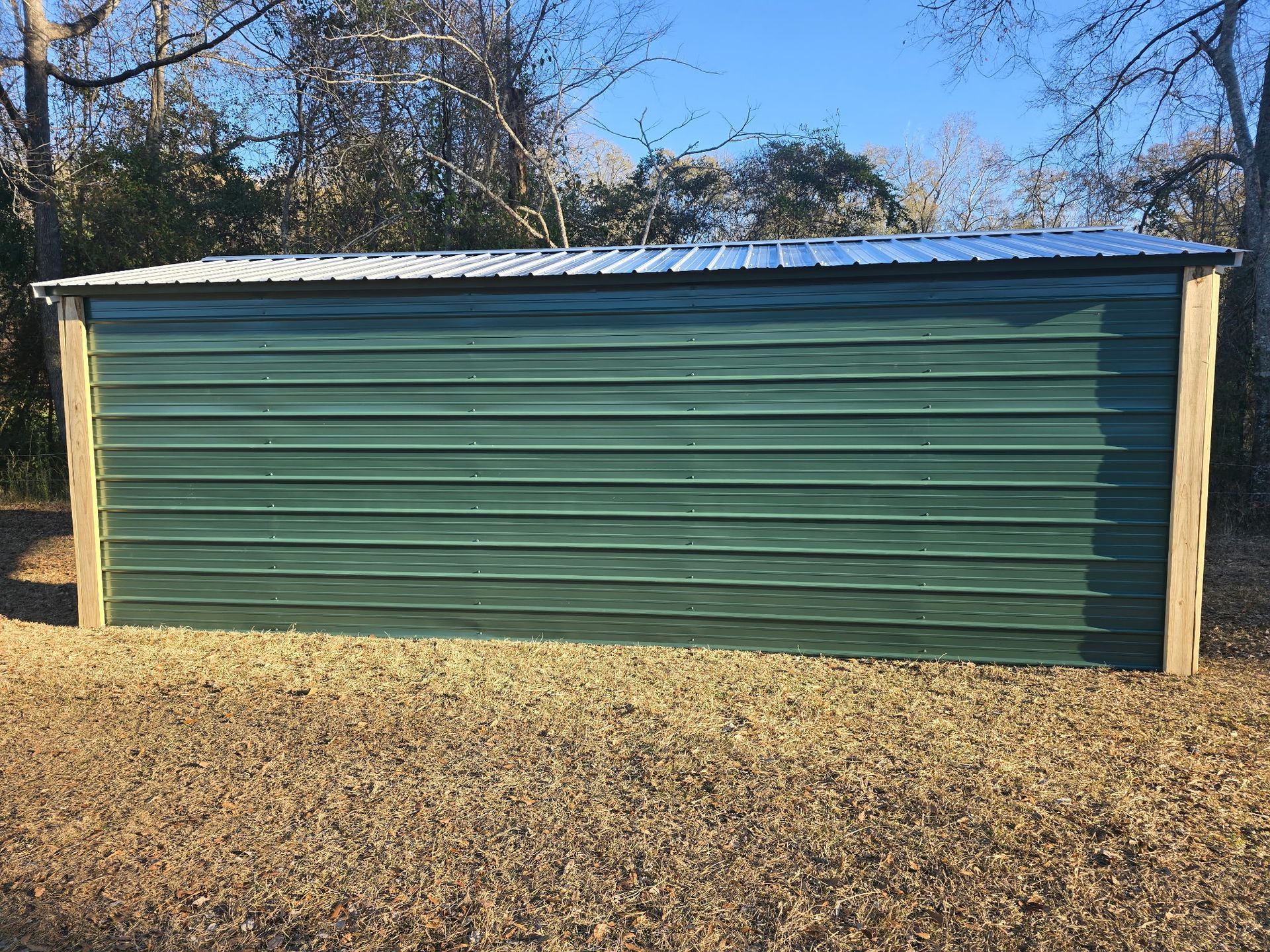 Green metal storage shed with a silver roof in a grassy area.