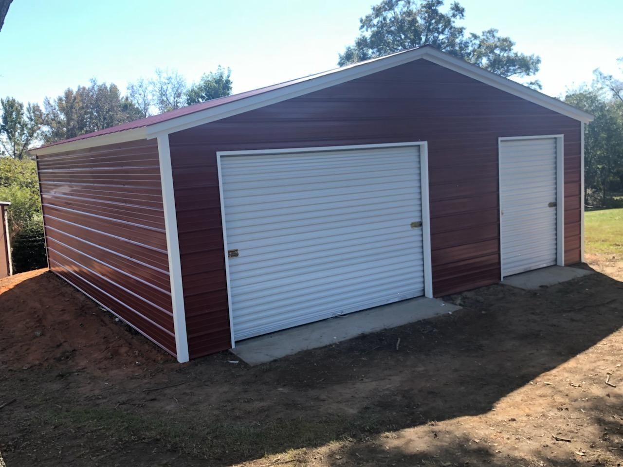 A red garage with two white garage doors is sitting on top of a dirt hill.