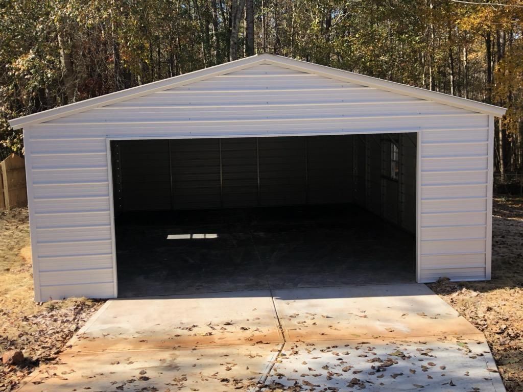 A white garage with a concrete driveway and trees in the background