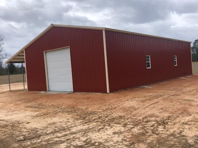 A red barn with a white door is sitting in the middle of a dirt field.