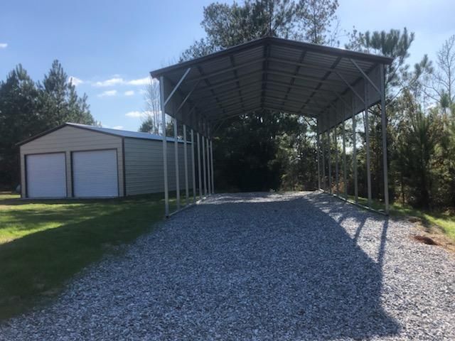 A carport is sitting next to a garage on a gravel road.