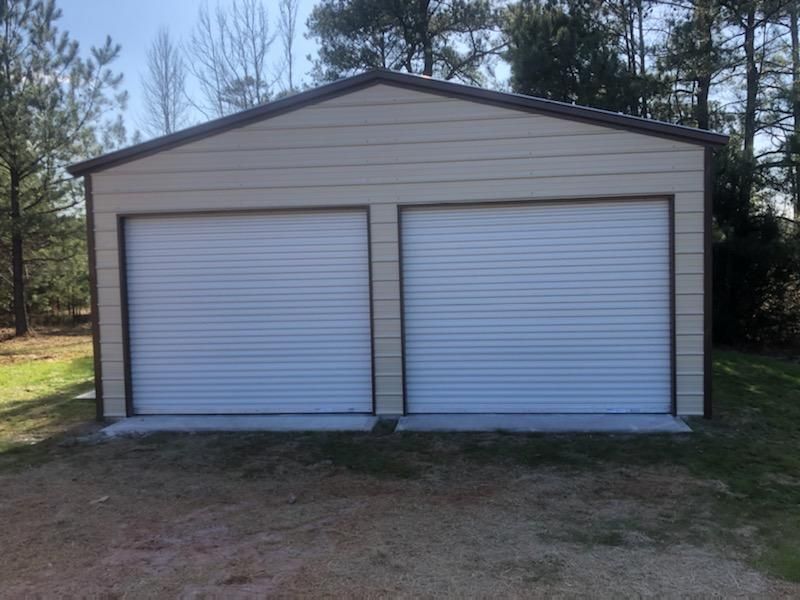 A metal garage with two white garage doors is sitting in the middle of a grassy field.