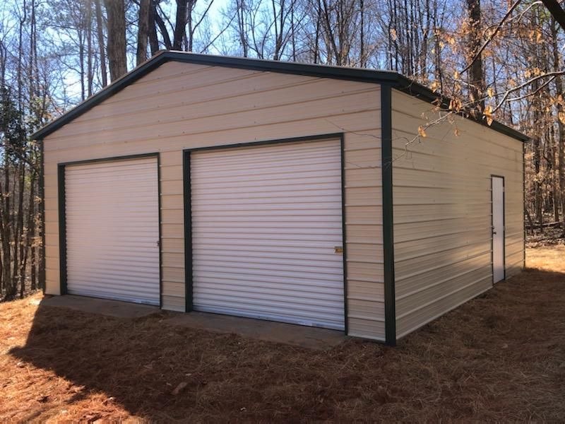 A metal garage with two garage doors is sitting in the middle of a field.