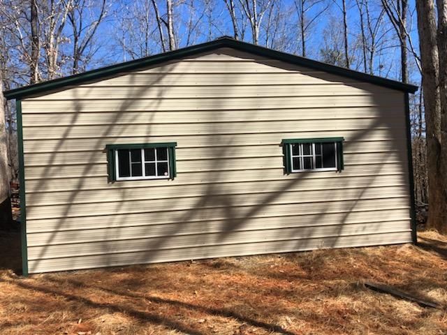 A garage with two windows on the side of it in the woods.