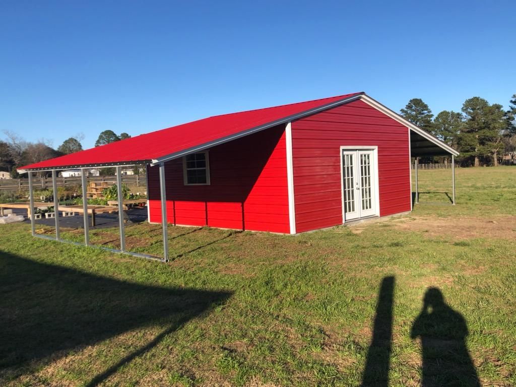 A red building with a white door and a red roof is in a grassy field.