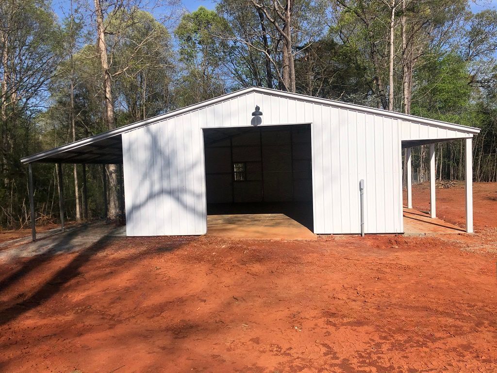 A white garage with a porch is sitting in the middle of a dirt field.