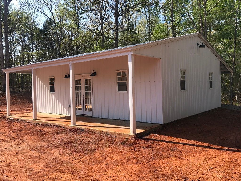 A white house with a porch in the middle of a dirt field.