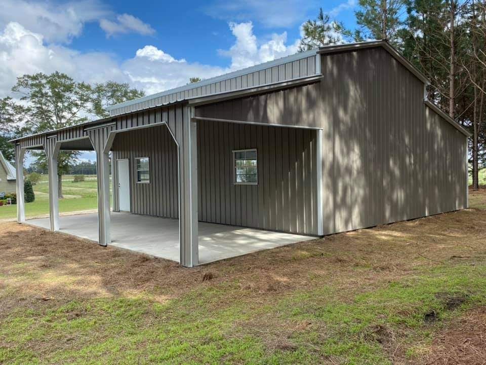 A large metal building with a porch and a garage is sitting in the middle of a grassy field.