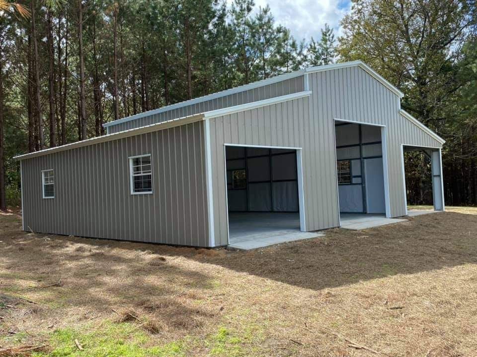 A large metal building with two garage doors is sitting in the middle of a field.