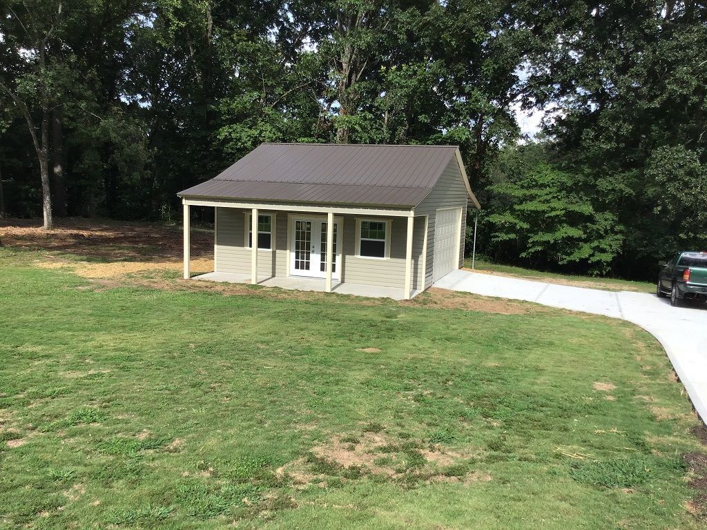 A small house with a porch is sitting on top of a lush green field.