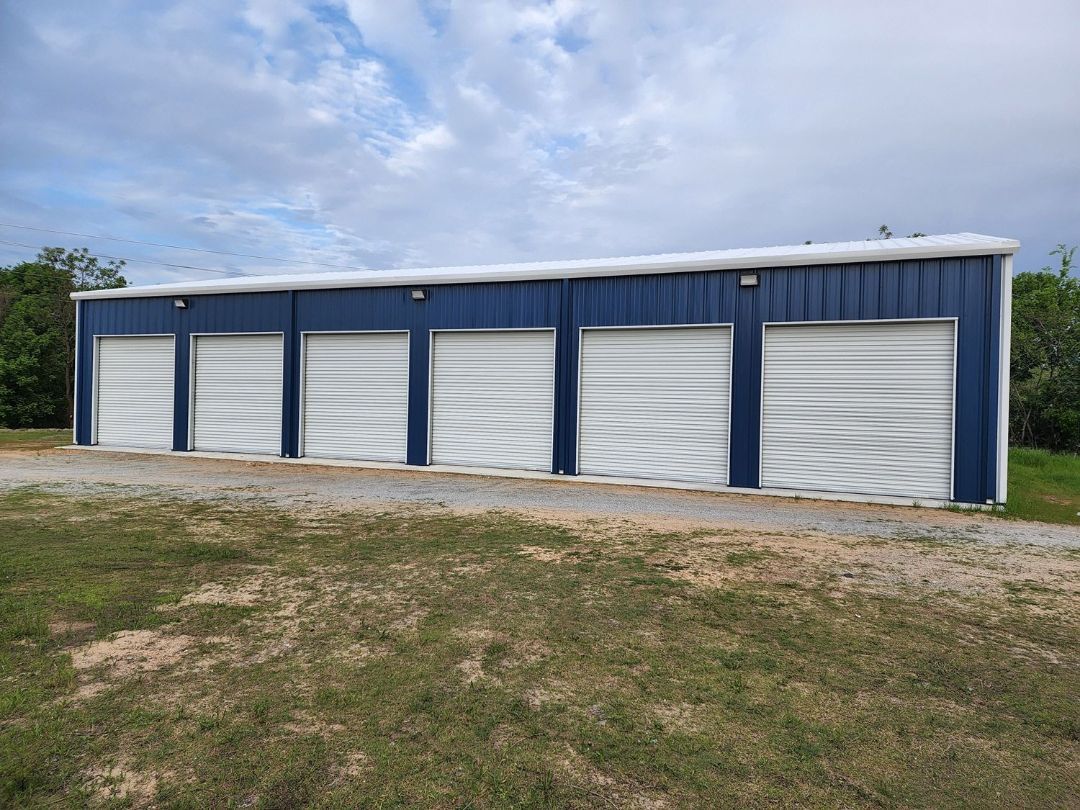 A large building with a lot of garage doors is sitting in the middle of a grassy field.
