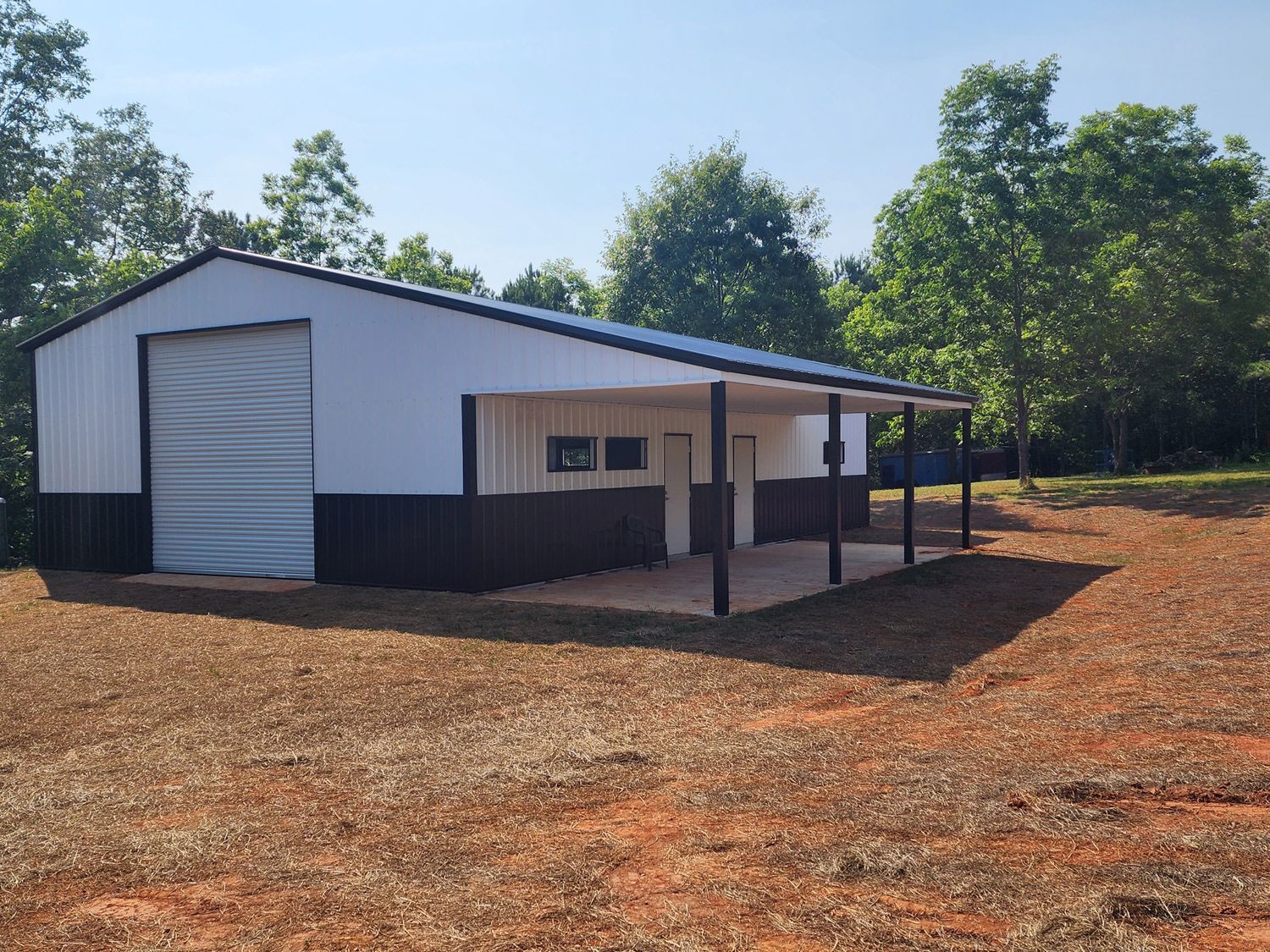 A white and black building with a porch in the middle of a dirt field.