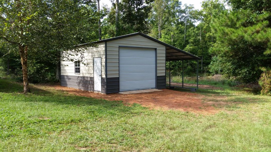 A small metal garage with a canopy is sitting in the middle of a grassy field.