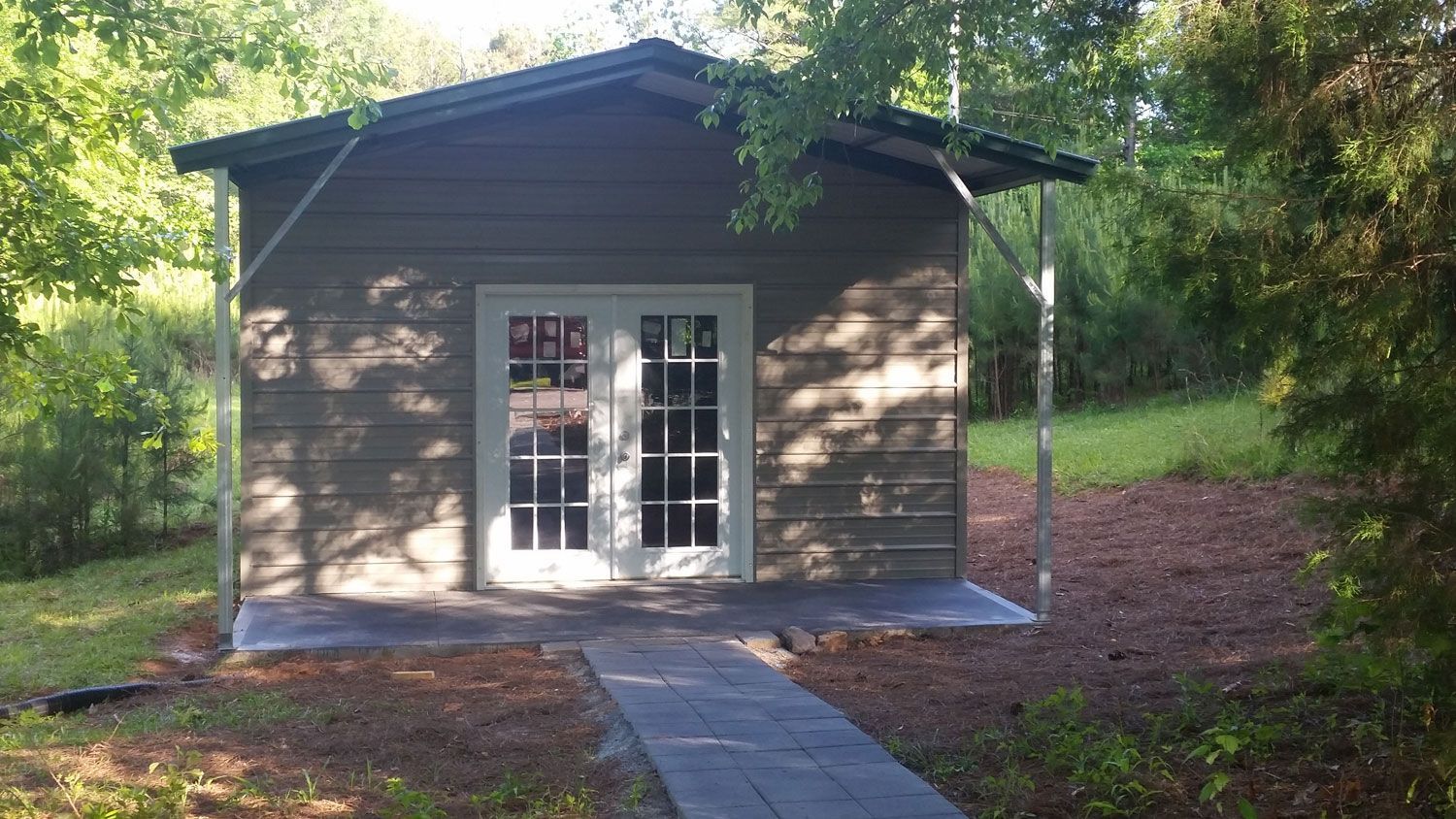 A small house with a walkway leading to it is surrounded by trees.