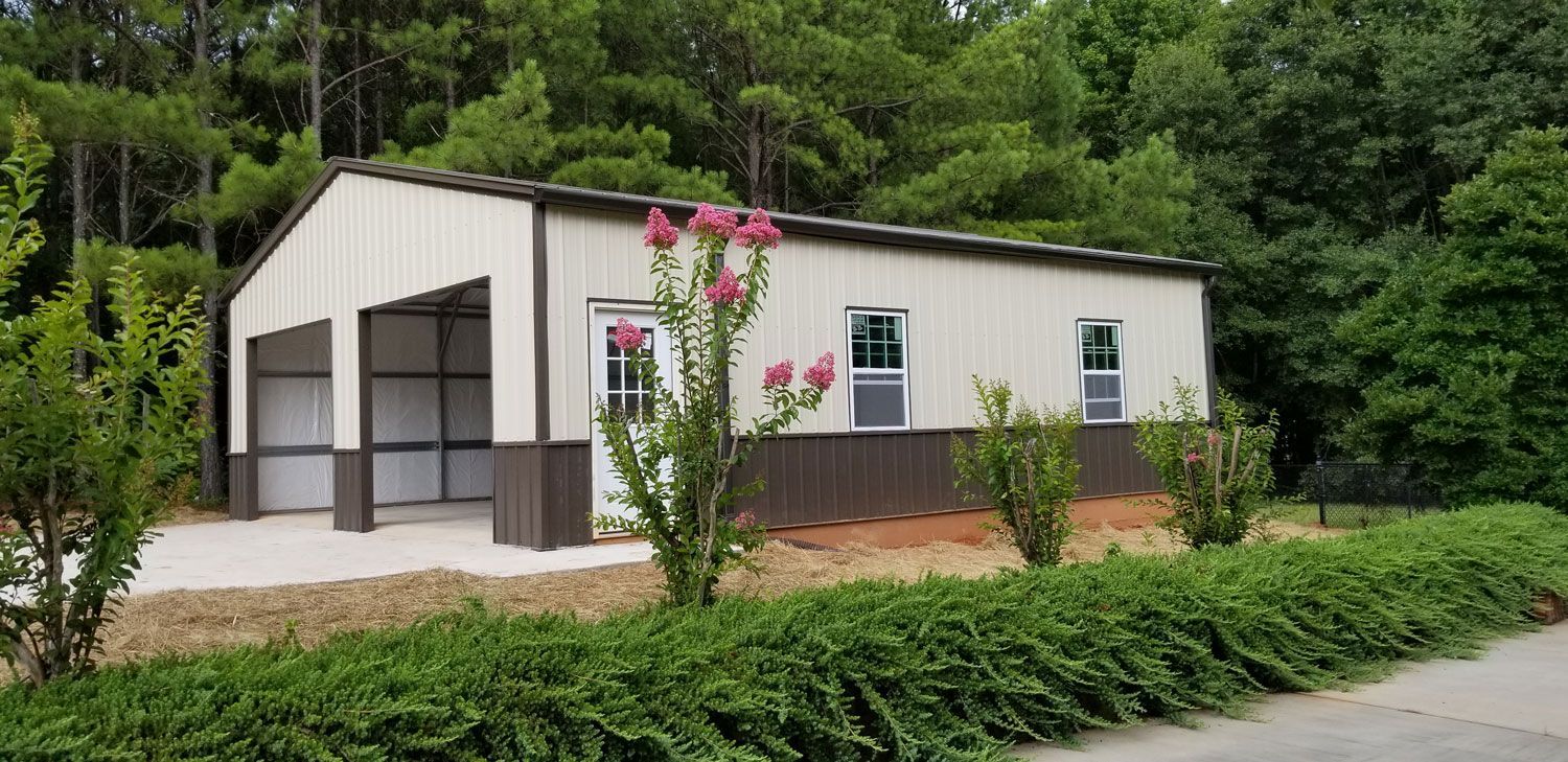 A white and brown building with a garage and trees in the background.