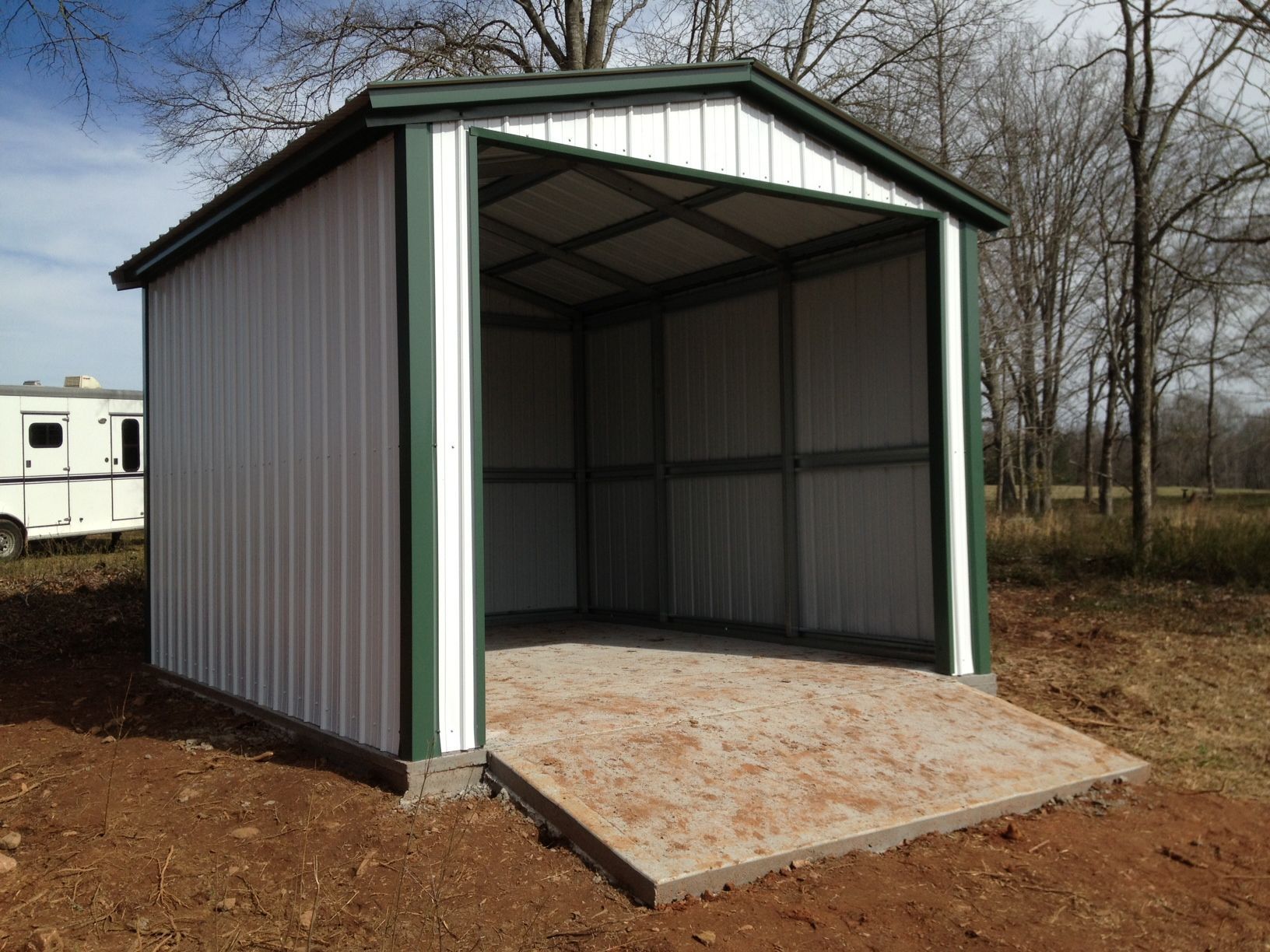 A white and green shed with a trailer in the background