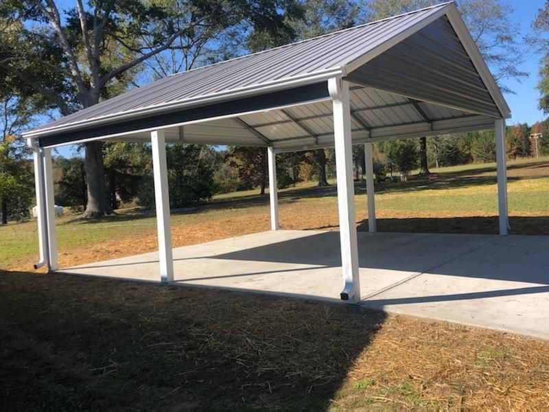 A carport with a gray roof and white posts in a park.