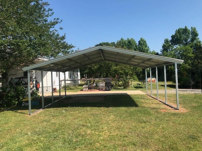 A metal carport is sitting in the middle of a lush green field.