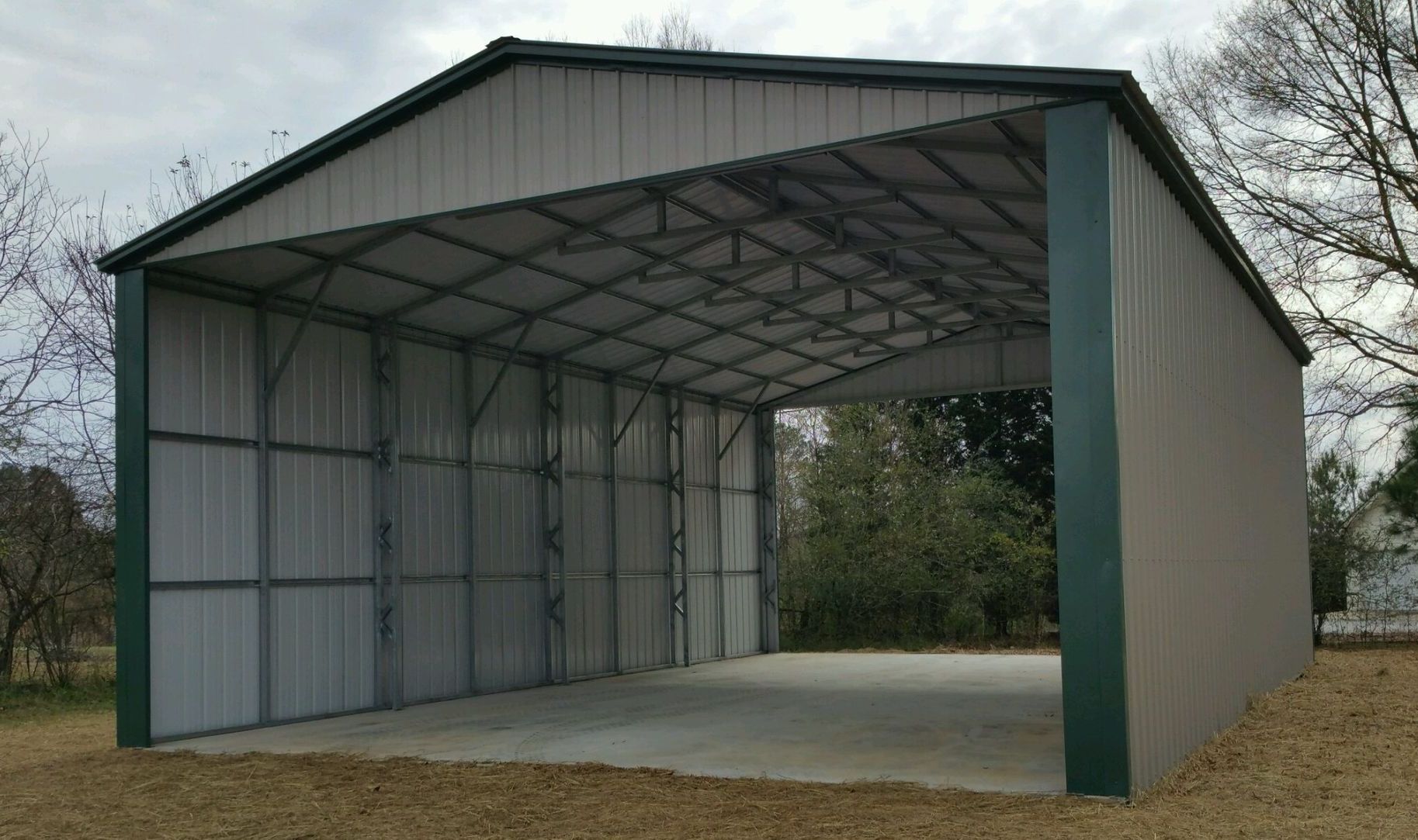 A large metal garage with a green roof is sitting on top of a dirt field.