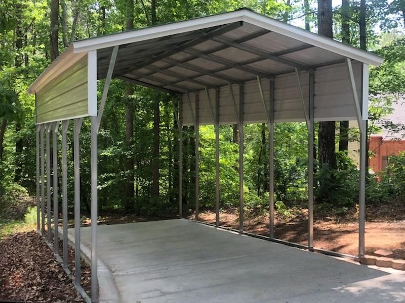 A metal carport is sitting on top of a concrete driveway surrounded by trees.