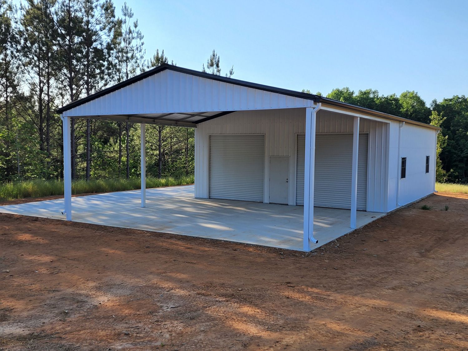 A white garage with a canopy over it is sitting in the middle of a dirt field.